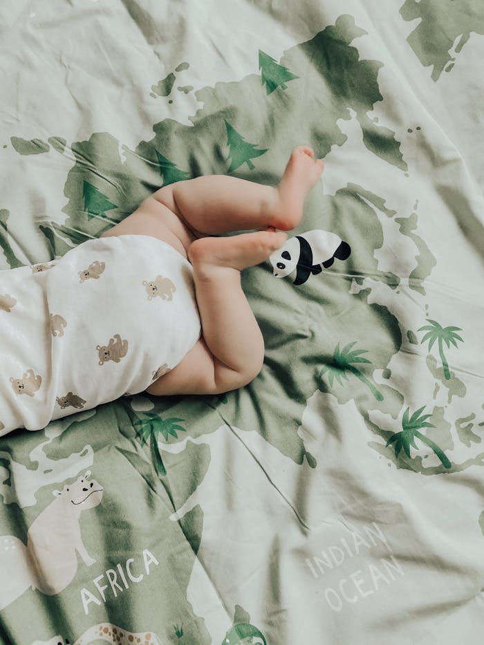 A baby on a printed blanket featuring animals and geographical names, creating a cute and cozy scene.