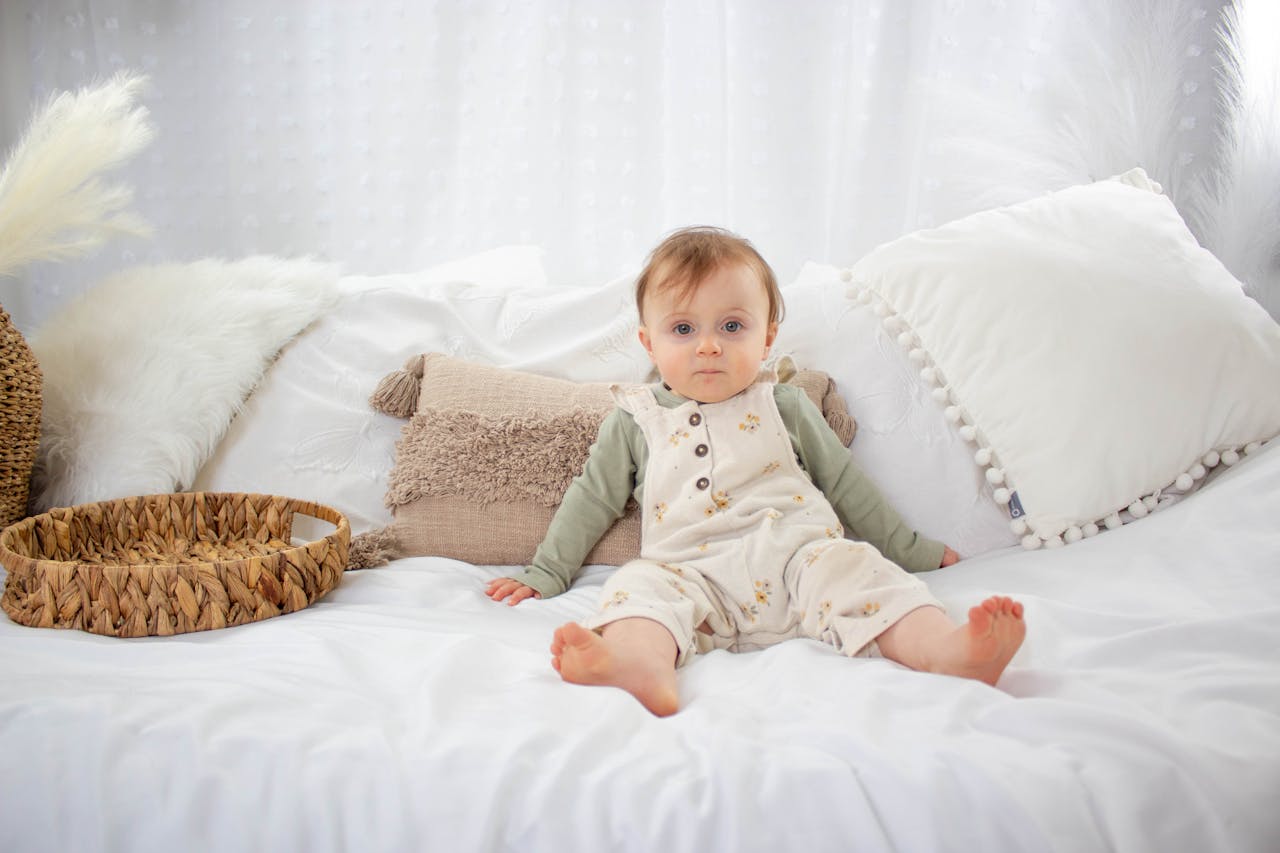 Cute baby sitting barefoot on a cozy bed with soft pillows, creating a comforting scene.