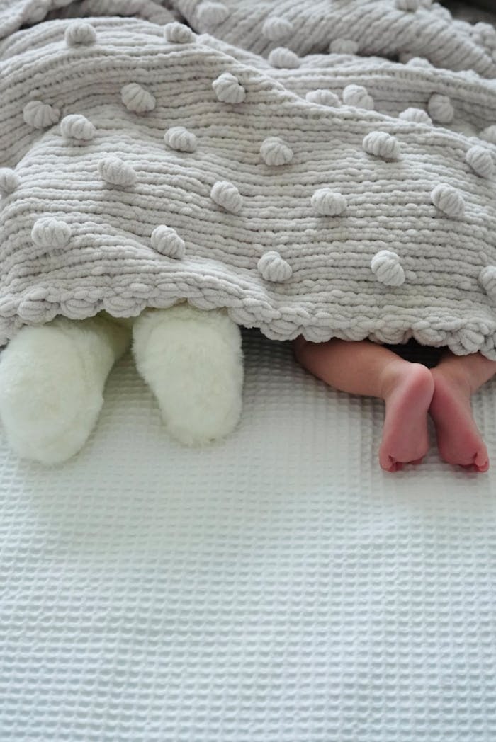 Adorable baby feet and toy peeking from under a cozy textured blanket, creating a cute and warm scene.