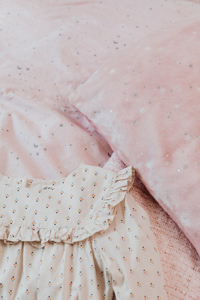 Delicate baby dress on soft pink star-patterned bedding.